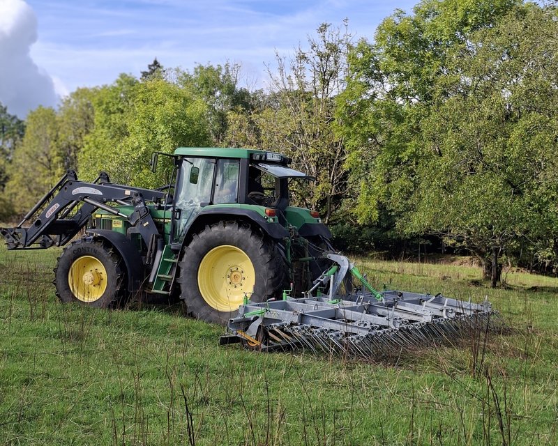 Ein Traktor bearbeitet eine Weidefläche mit einem Striegel.